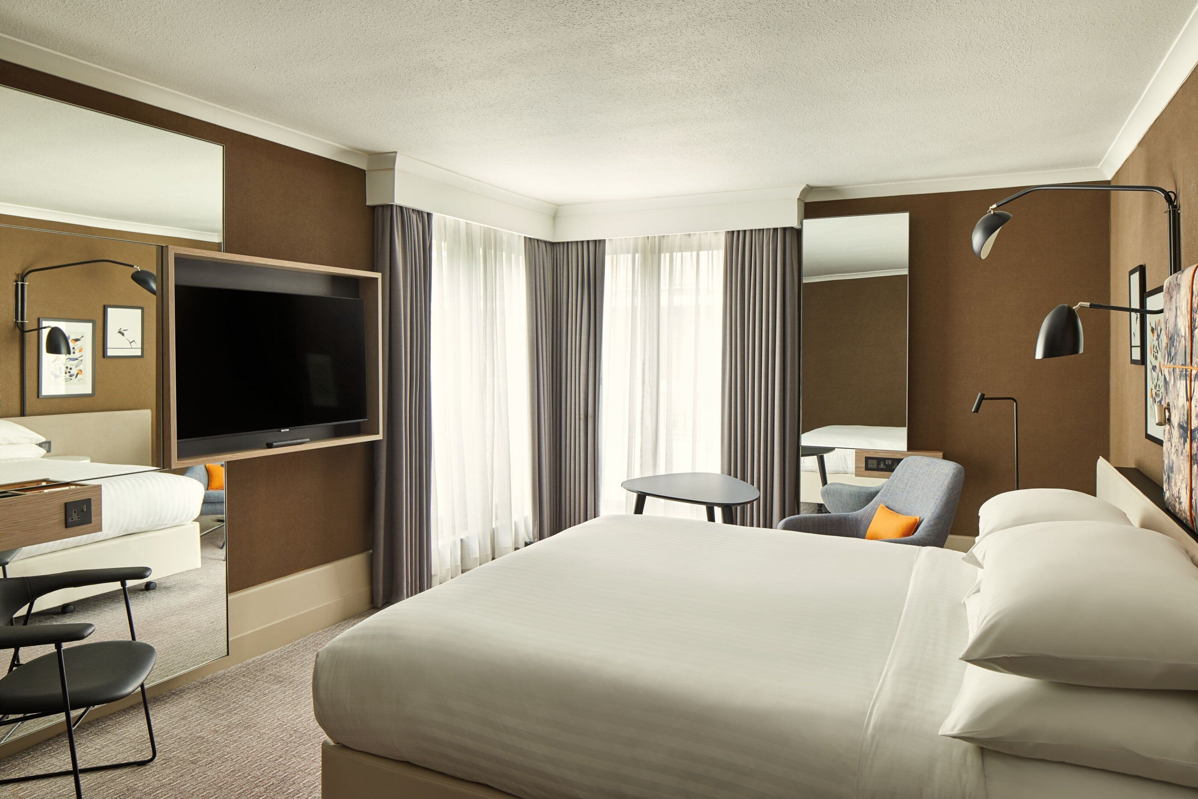 A hotel room with a large bed, a flat-screen TV, a desk with a chair, a small table, and a chair.