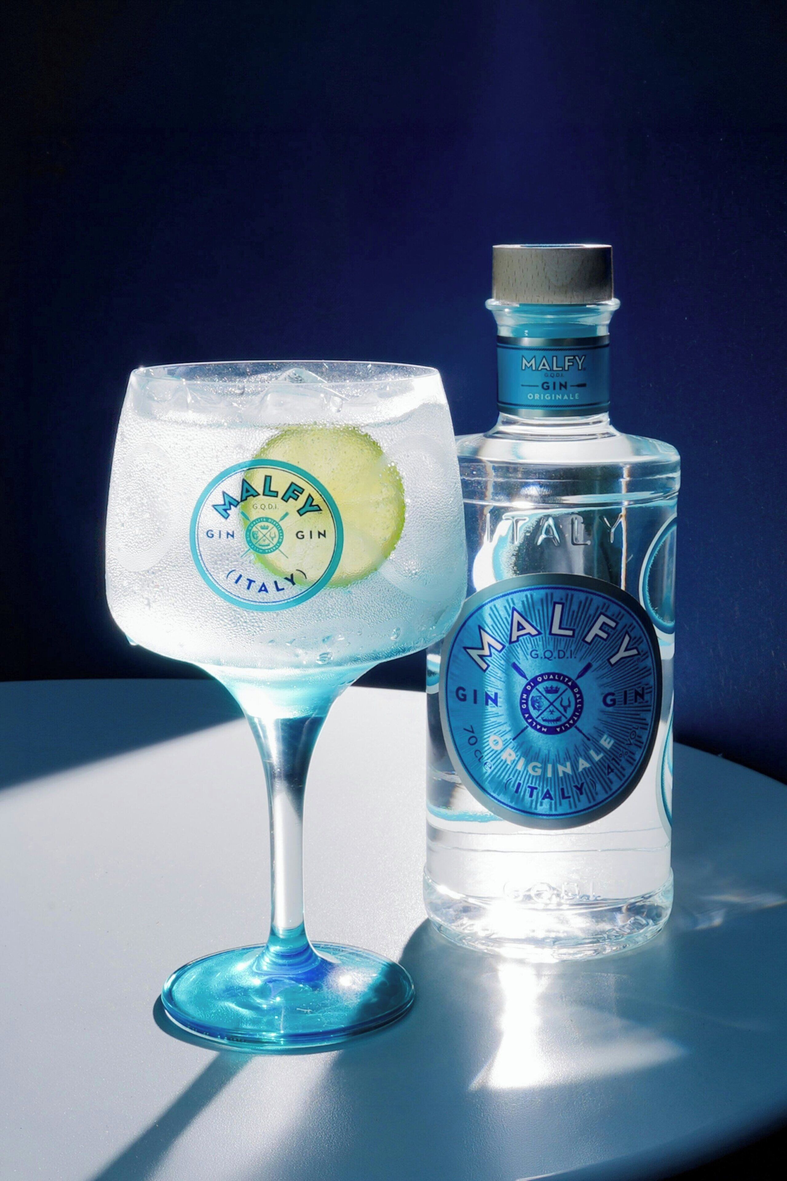 A clear glass with a lime slice and a bottle of Malfy gin.