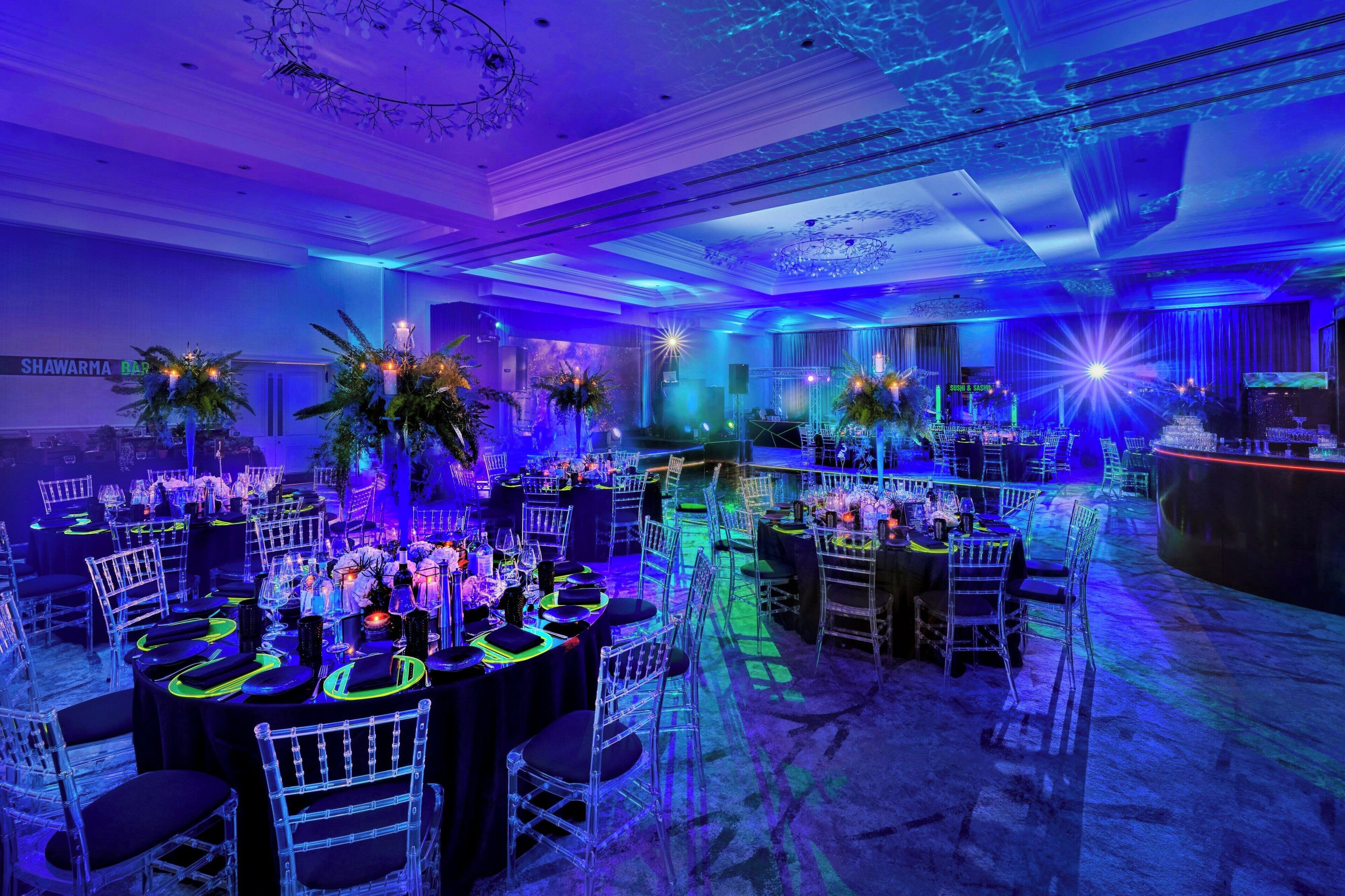 A banquet hall with round tables, clear chairs, and floral centerpieces.