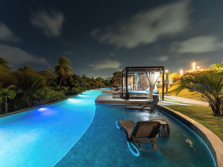 Piscina com espreguiçadeiras e área de estar coberta à noite.