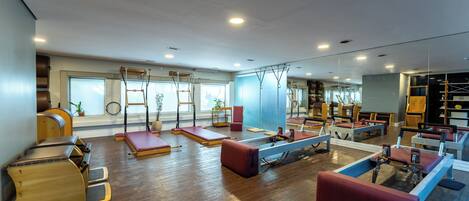 A spacious gym with various exercise equipment, including Pilates reformers and yoga mats.