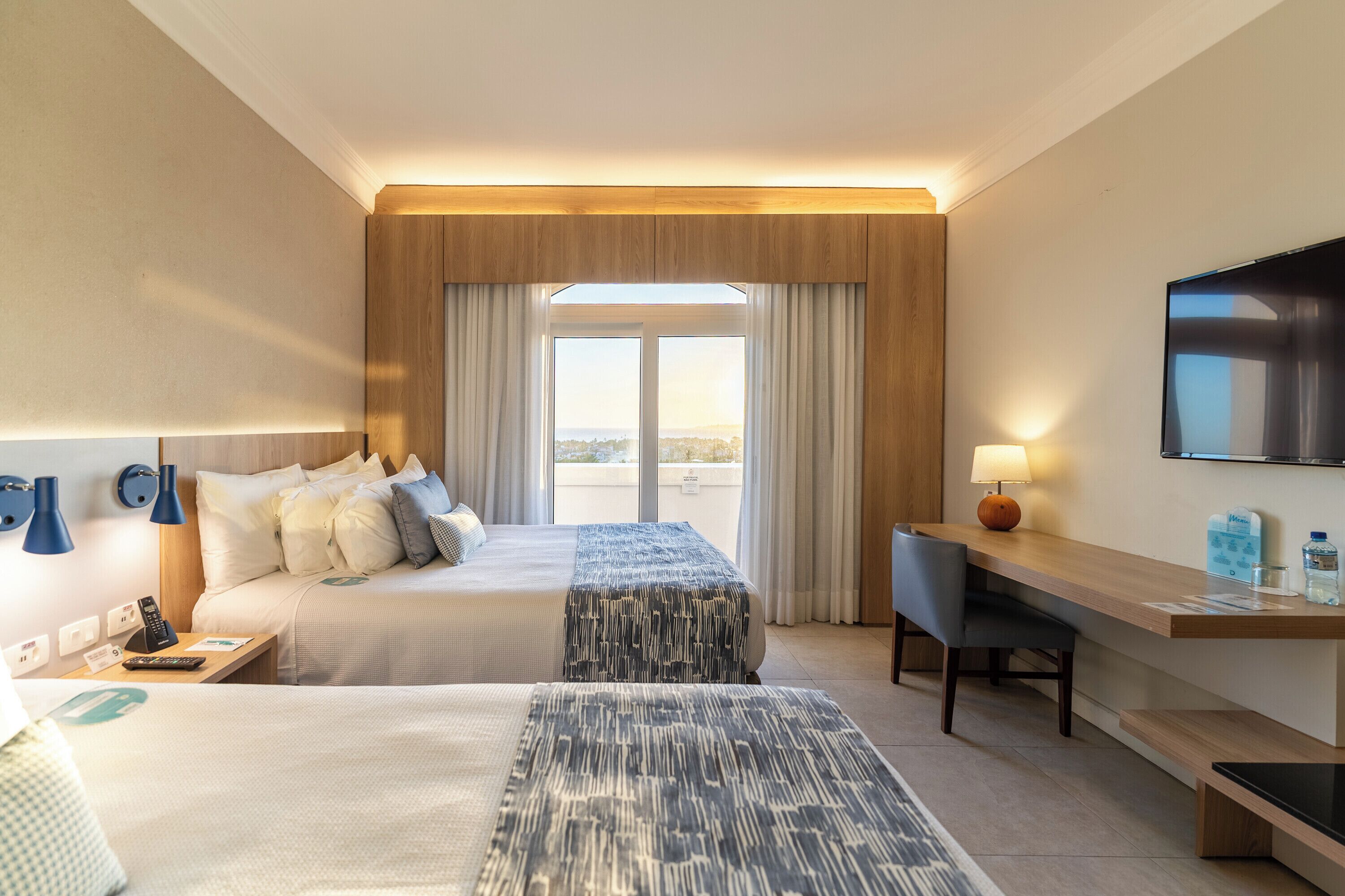A hotel room with a bed, a desk, a chair, a TV, and a window with curtains.