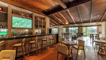 Uma área de bar com teto de madeira, banquetas e uma televisão exibindo uma partida esportiva.