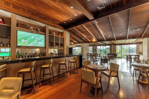 Un espace bar avec un plafond en bois, des tabourets de bar et un téléviseur diffusant un événement sportif.