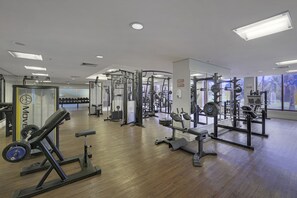 Une salle de sport équipée de divers appareils d’exercice, dotée d’un plancher en bois et de grandes fenêtres.