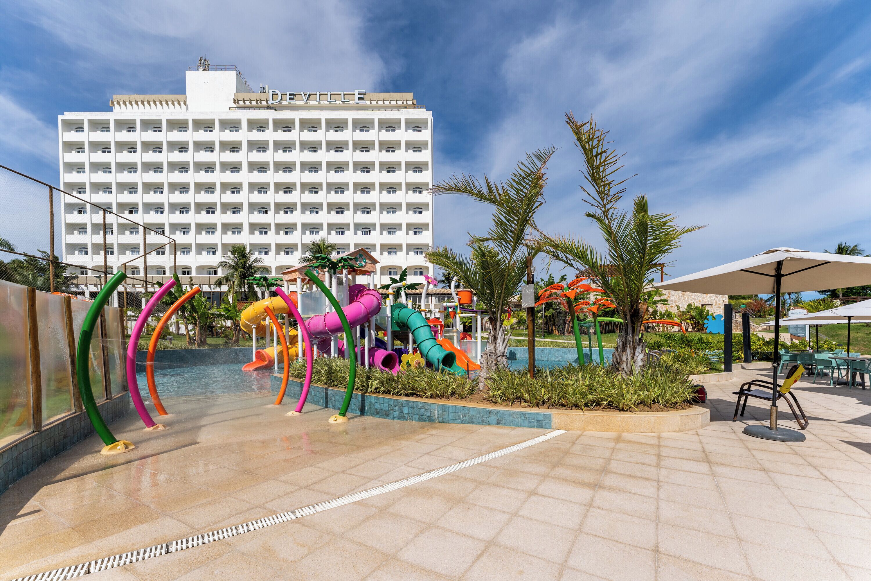 Un hôtel doté d’un grand bâtiment, d’un espace piscine avec des toboggans colorés et d’un espace extérieur aménagé pour se d étendre.