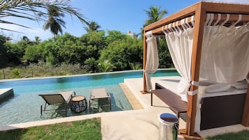 Relax by the serene pool surrounded by lush greenery and a shaded pergola.