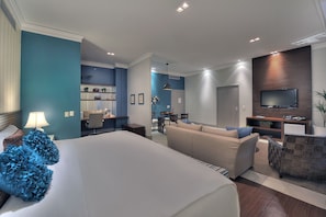A modern hotel room with a large bed, a sofa, a TV, and a dining area.