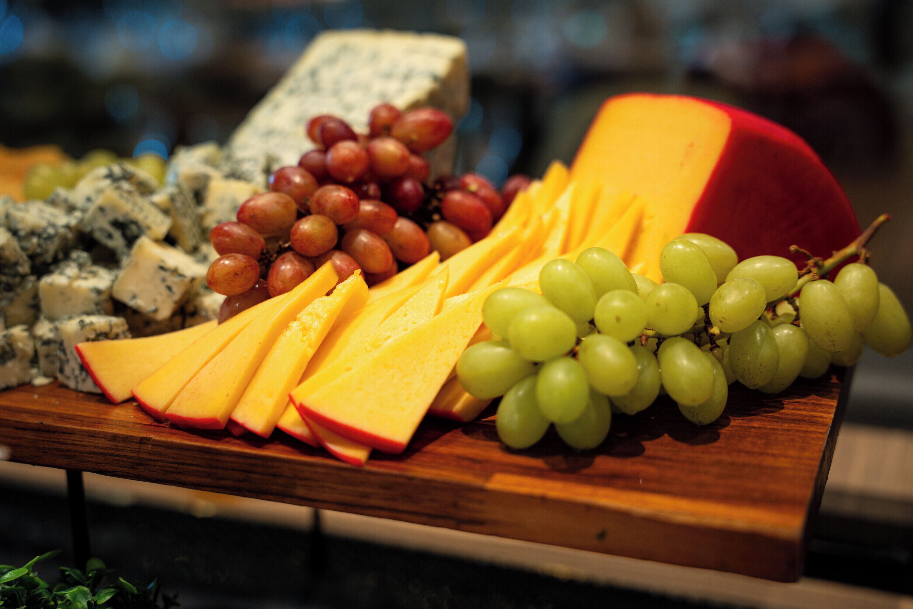Une planche en bois garnie de fromage, de raisins et de fromage bleu.