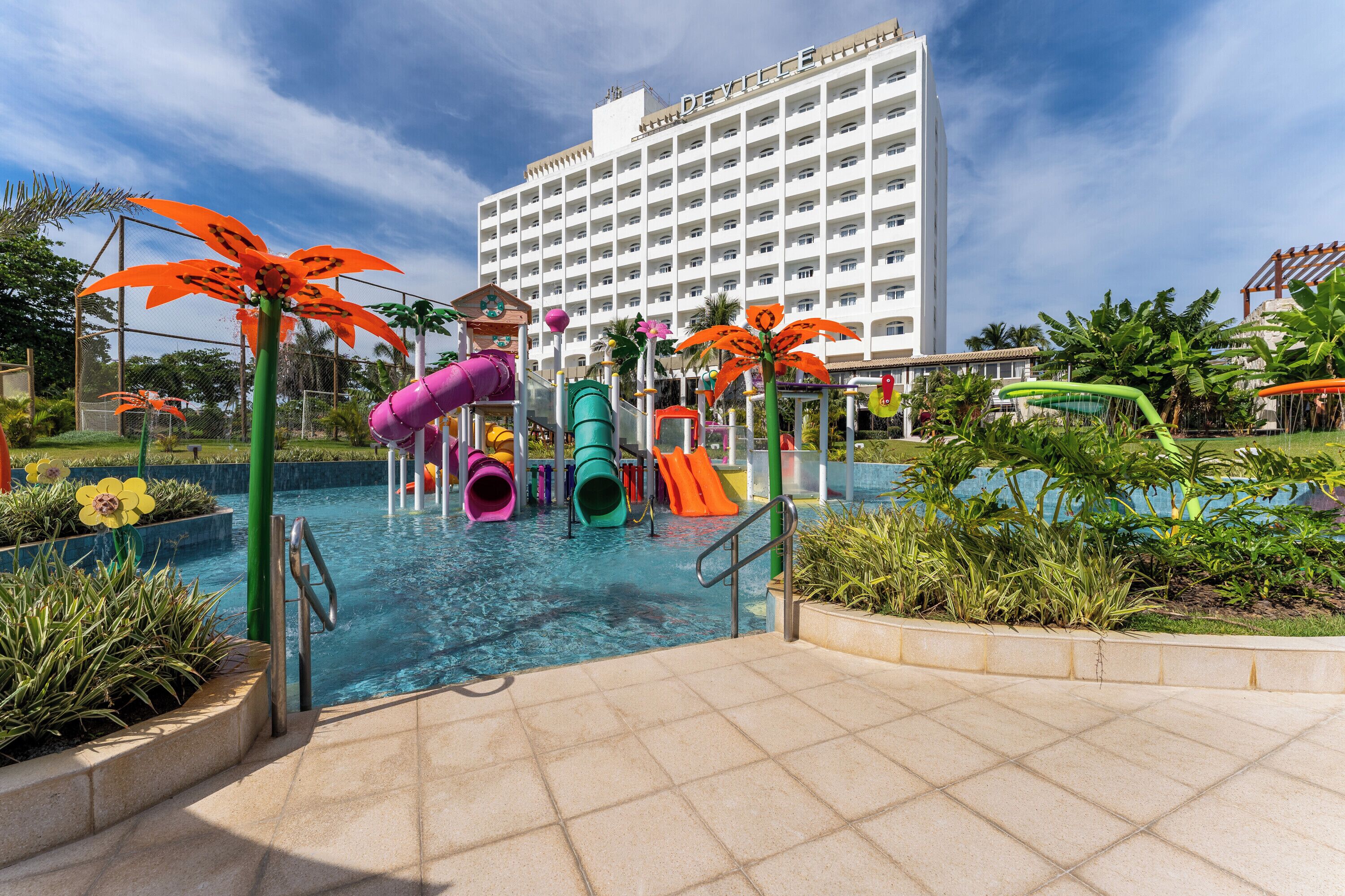 A hotel with a swimming pool area featuring a water play structure with slides and a multi-level play area.