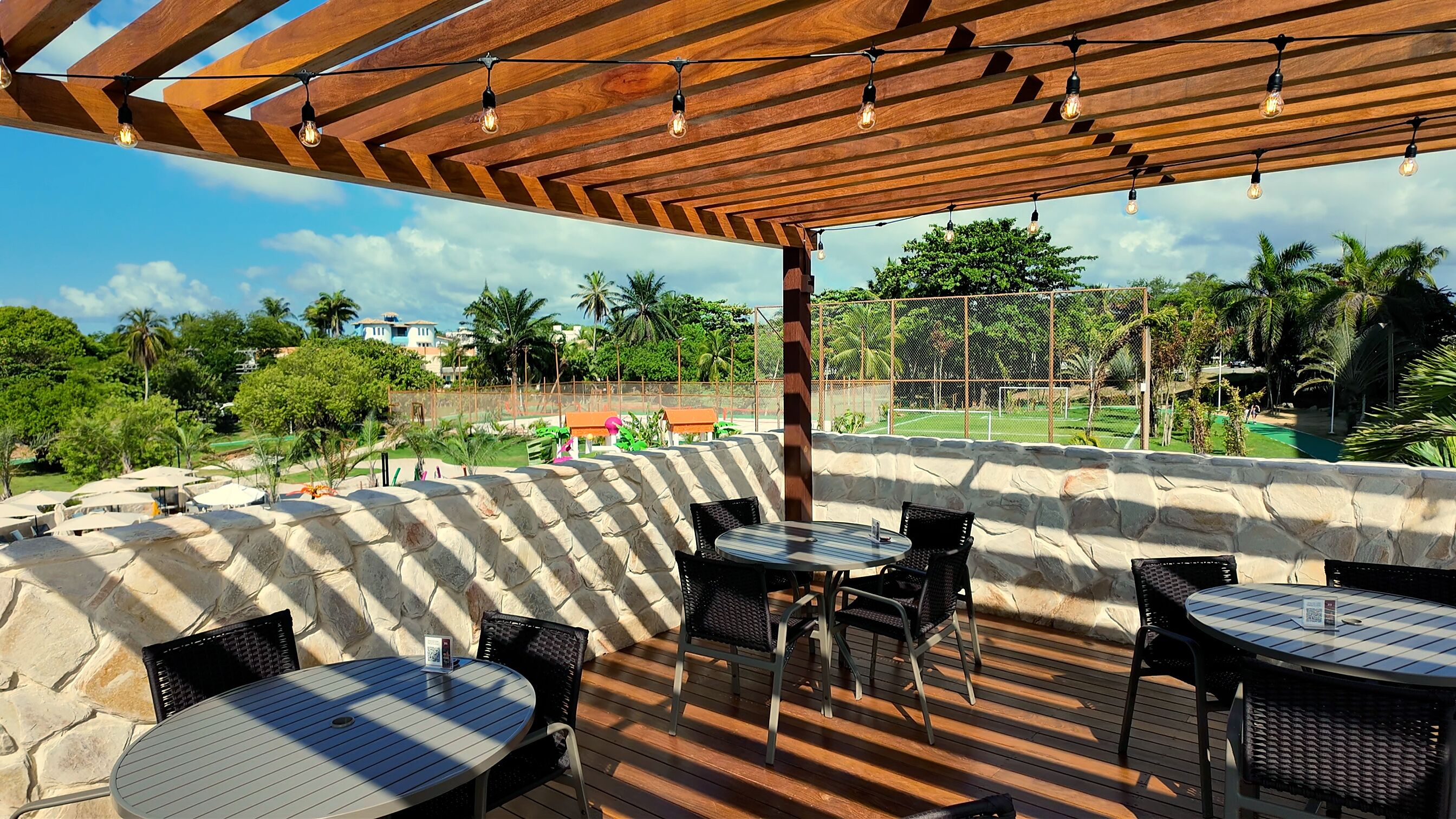 An outdoor patio area with stone walls, wooden pergola, and tables and chairs.
