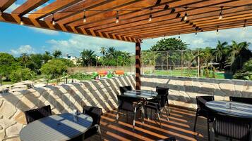 An outdoor patio area with stone walls, wooden pergola, and tables and chairs.