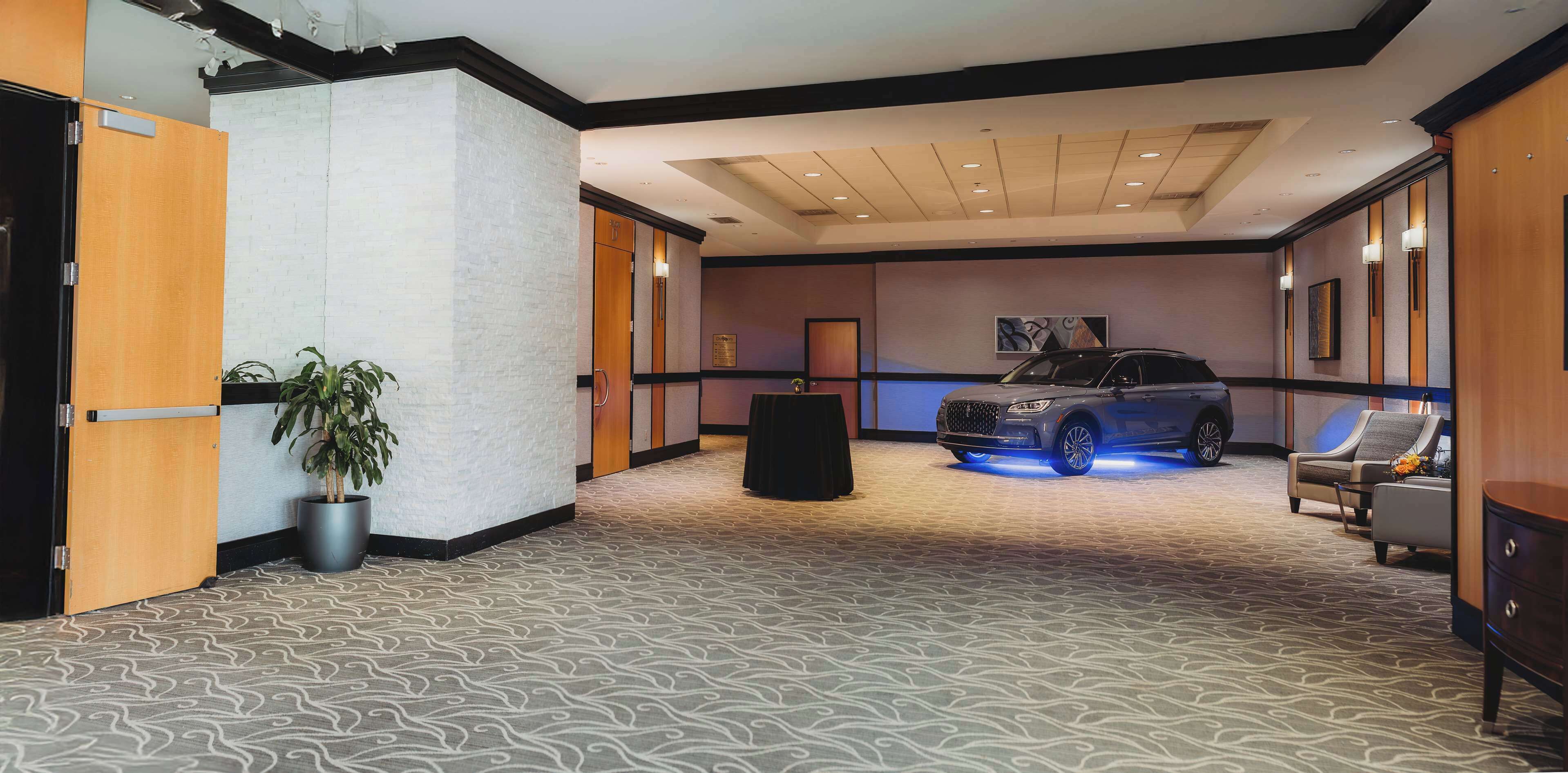 Un vestíbulo de hotel con alfombra estampada, una planta en maceta, un coche con luces azules y una zona de estar.