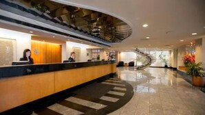 A hotel reception area with a curved reception desk, a staircase, and a polished marble floor. - Somerset Inn, WorldHotels Distinctive (Troy)