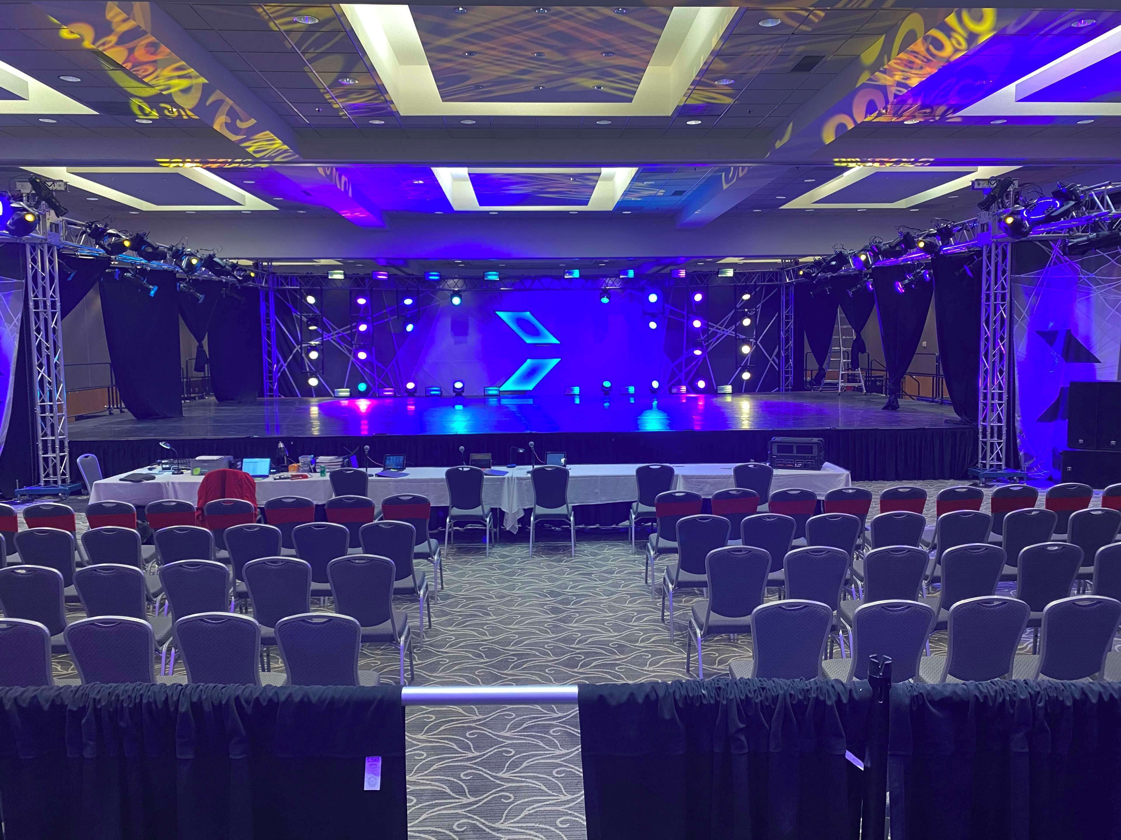A conference room with a stage, rows of chairs, and a carpeted floor.