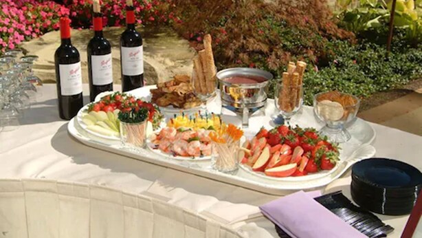 A table set outdoors with wine bottles, a fruit platter, and bread. - Somerset Inn, WorldHotels Distinctive (Troy)