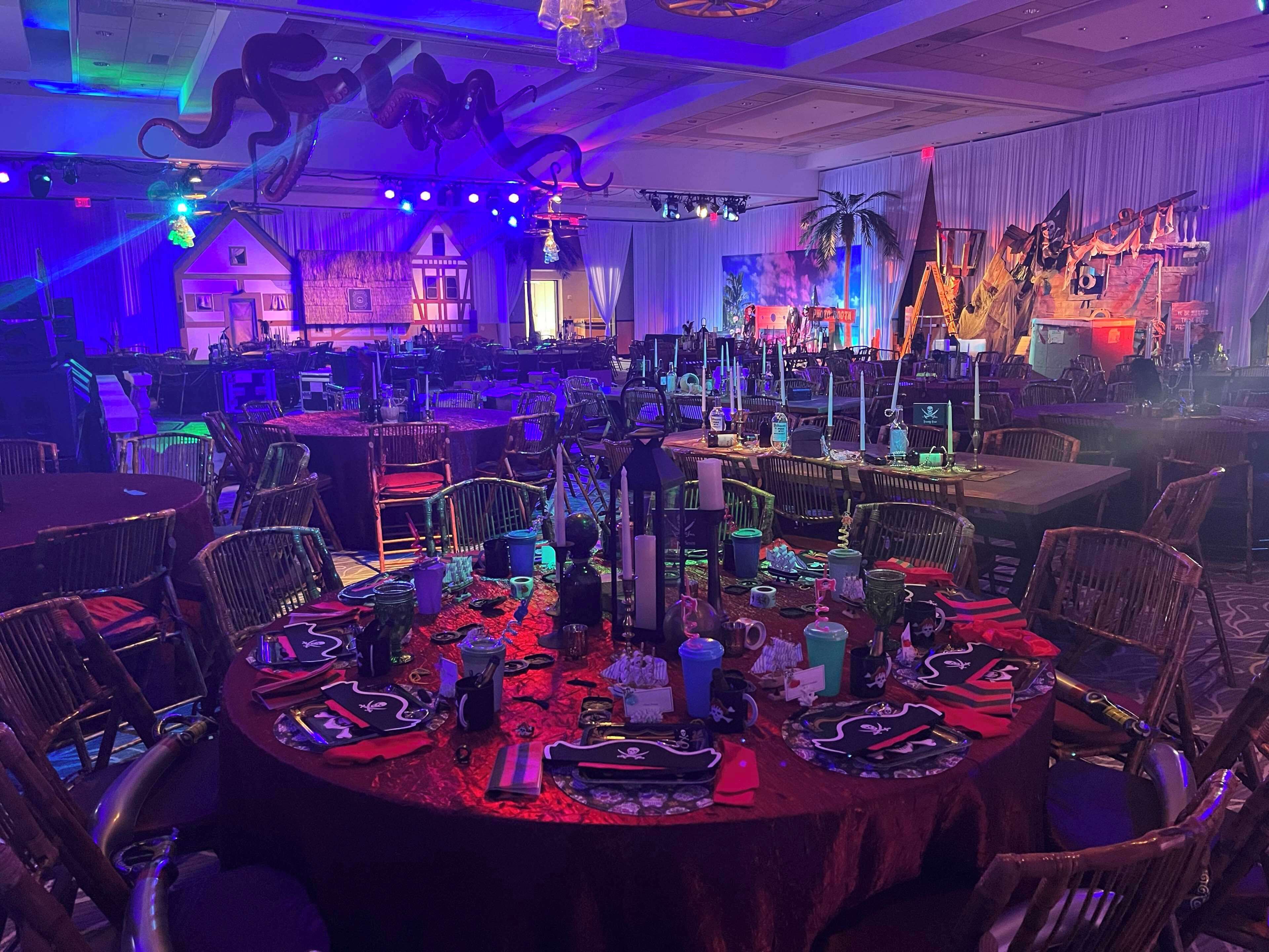 A banquet hall with round tables, chairs, and a stage with a backdrop.