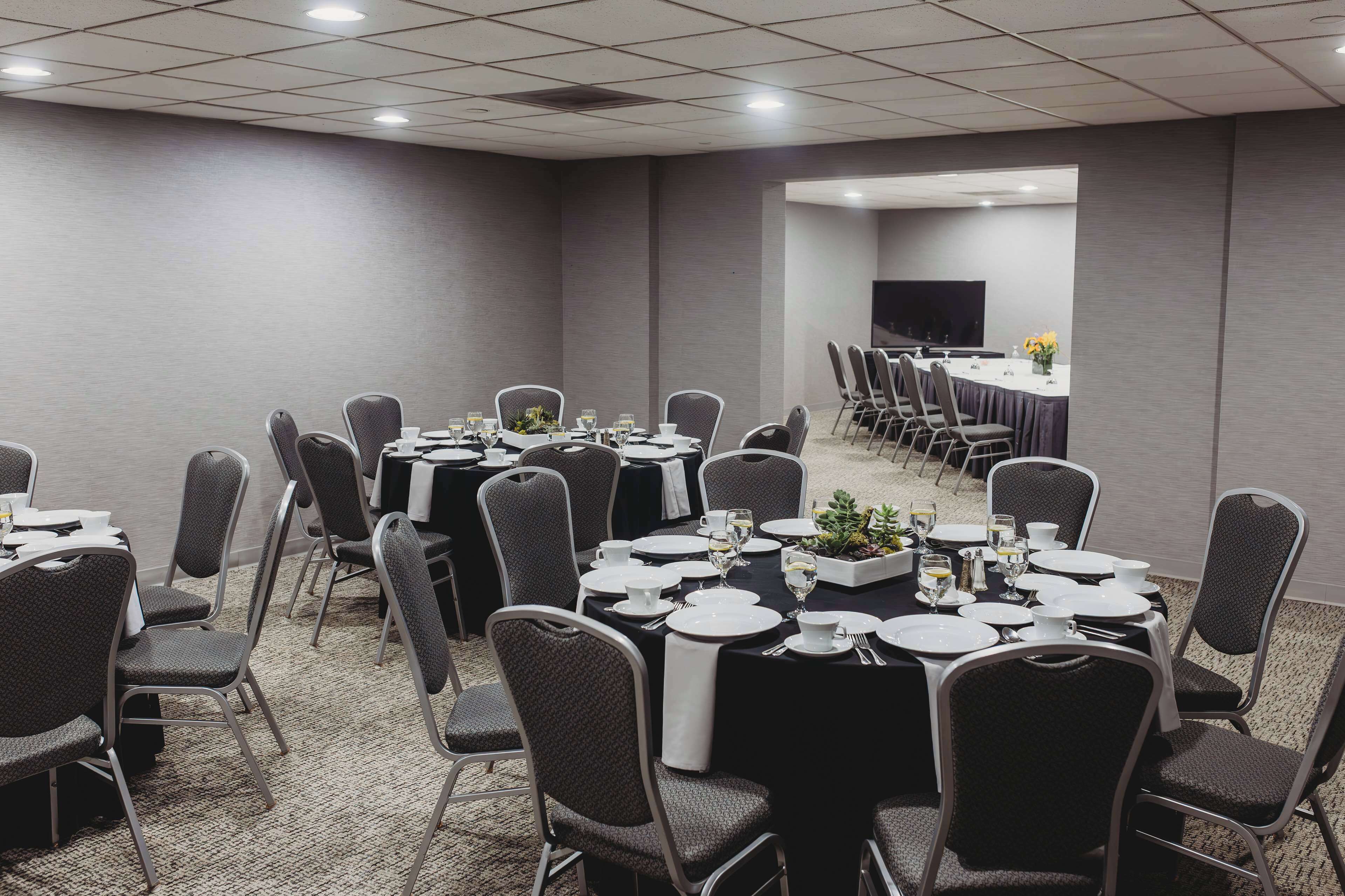 A conference room with multiple tables set for dining, equipped with chairs and tables, and a television screen.