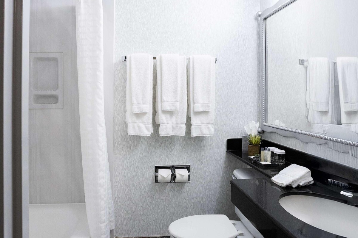 A modern bathroom with a shower, toilet, and sink. There are towels hanging on a rack and a mirror above the sink.