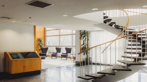 A modern lobby with a spiral staircase, seating area, and a reception desk. - Somerset Inn, WorldHotels Distinctive (Troy)
