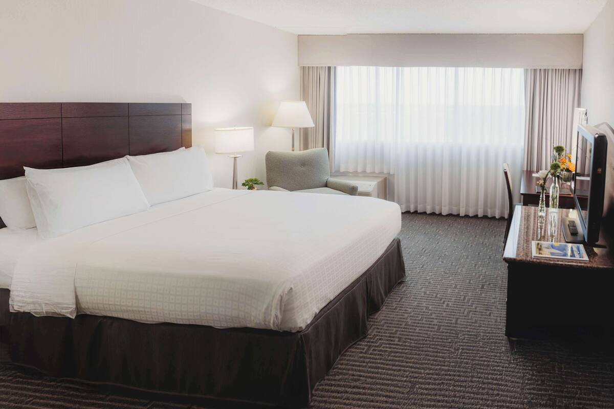 A hotel room with a large bed, two bedside tables with lamps, a desk with a TV, and a window with curtains.