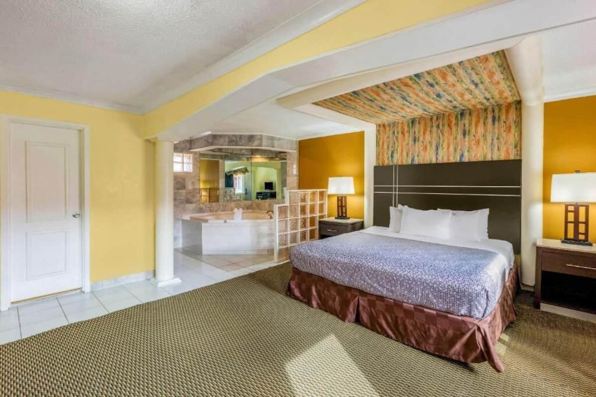 Habitación de hotel con cama, mesita de noche, lámpara, baño con ducha y vistas al exterior.