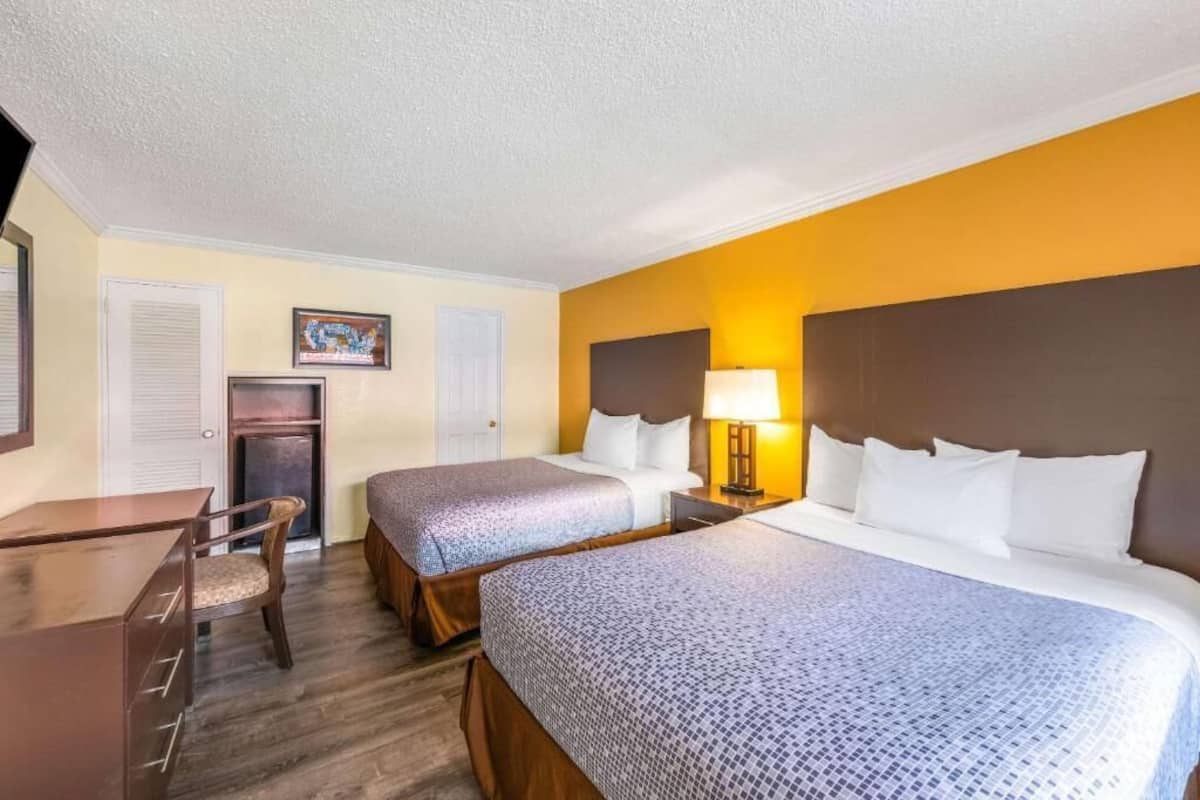 Una habitación de hotel con dos camas, un escritorio, una silla, un televisor y una lámpara.
