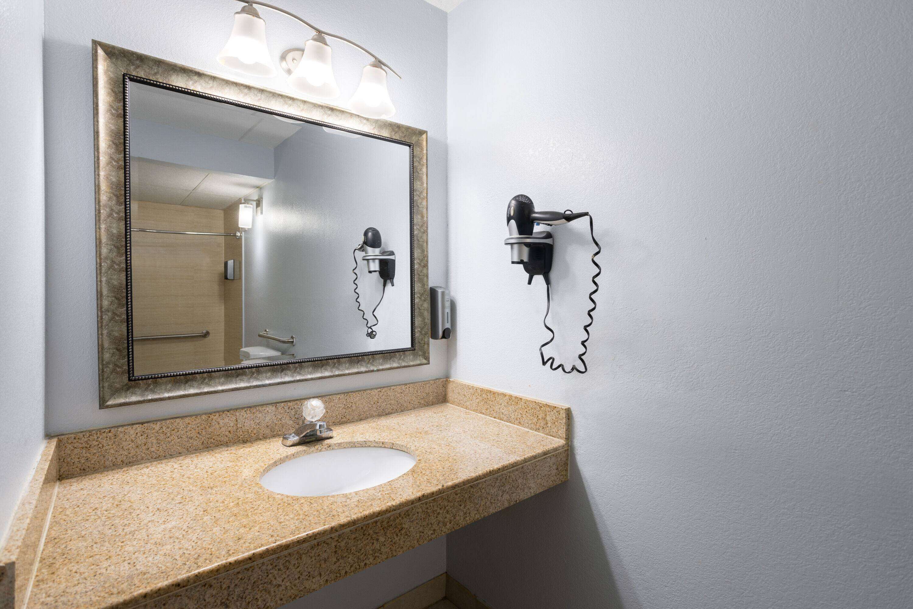 Een badkamer met een wastafel met een granieten blad, een spiegel met verlichting en een wandhaardroger.