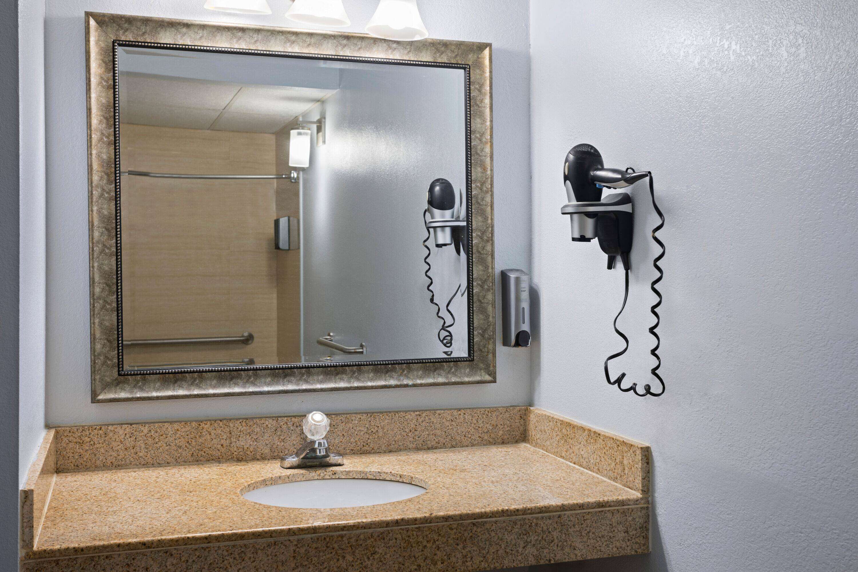 Un bany amb taulell de granat, un lavabo, un mirall amb marc decoratiu i un assecador de cabells penjat a la paret.