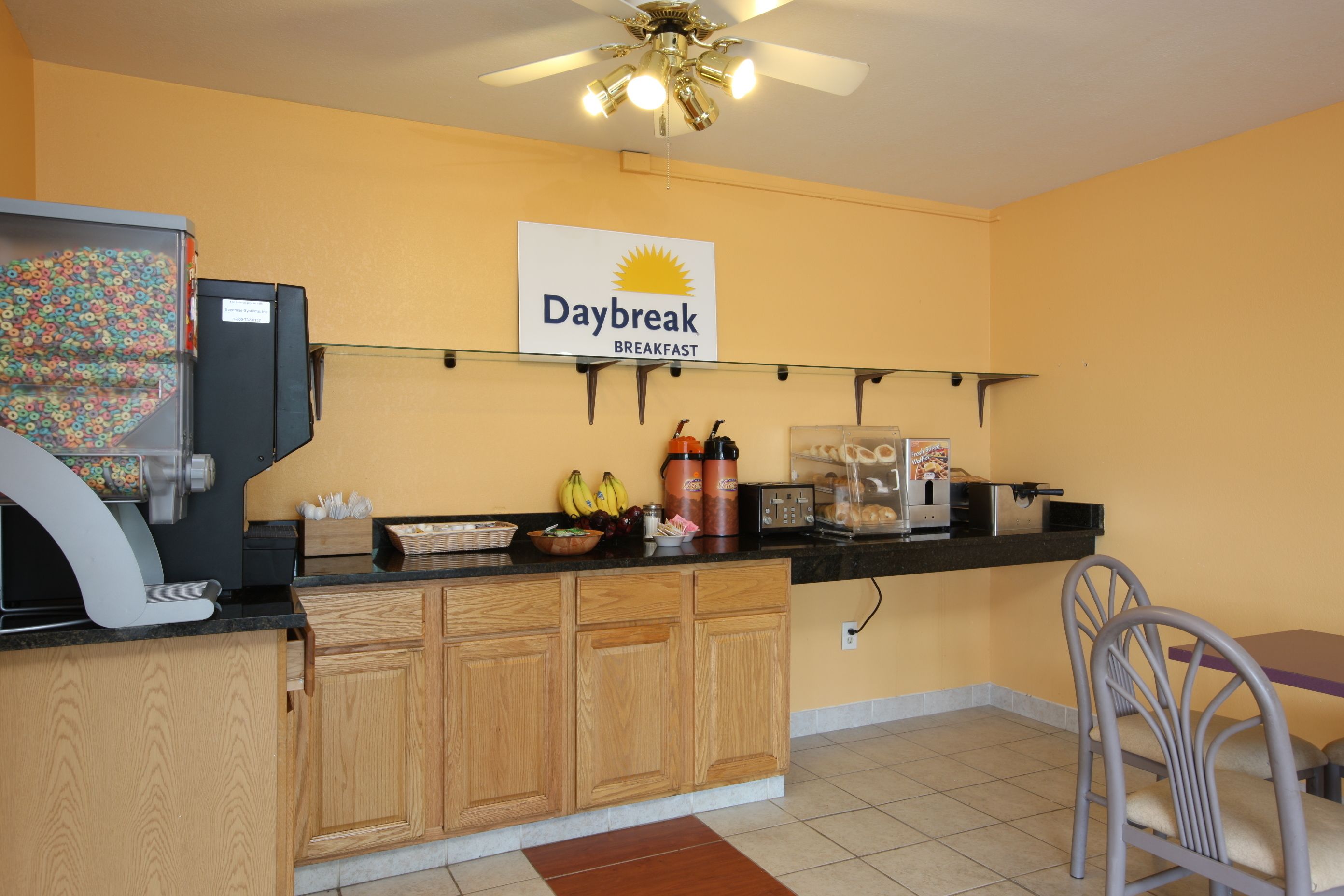 Una cocina con un cartel que dice 'Daybreak Breakfast', armarios de madera, una cafetera y un frutero.