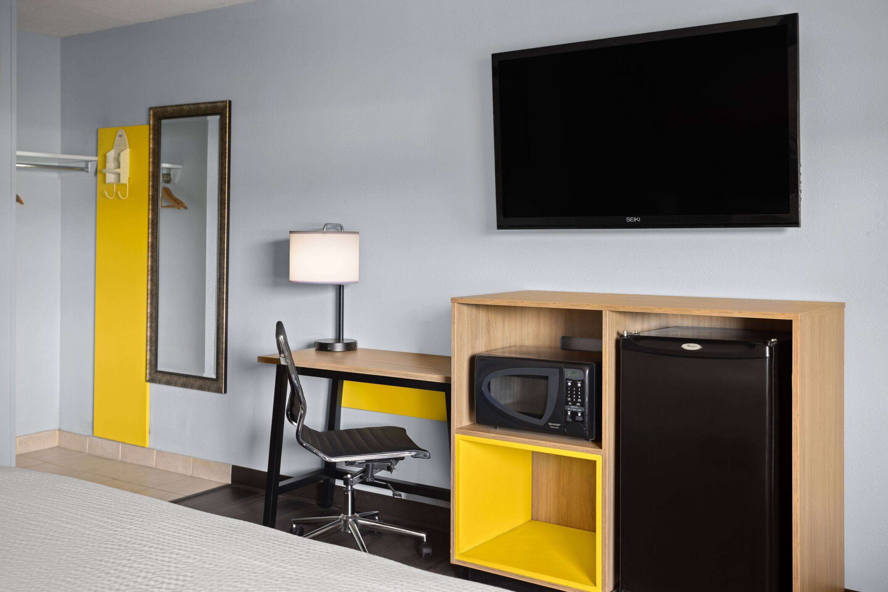 Ein Hotelzimmer mit einem Bett, einem Schreibtisch mit Stuhl, einem Fernseher, einer Mikrowelle und einem Kühlschrank.