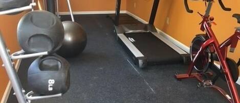 Un gimnasio con equipo de ejercicio, incluyendo una cinta de correr, elíptica y bicicleta estática.