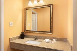 A bathroom with a granite countertop, a sink, a mirror, and a coffee maker. - Days Inn by Wyndham Queensbury/Lake George (Queensbury)