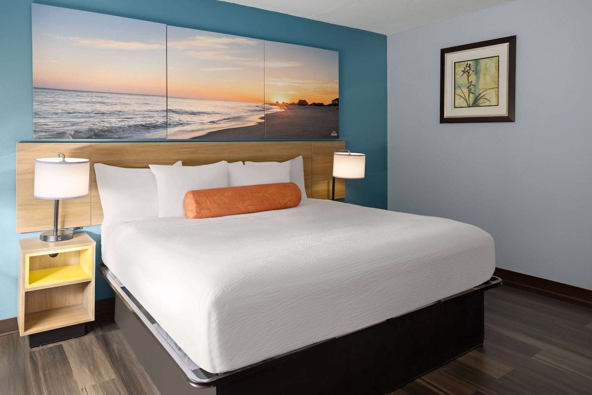A hotel room with a large bed, two bedside lamps, a nightstand, a framed picture on the wall, and a painting above the bed.