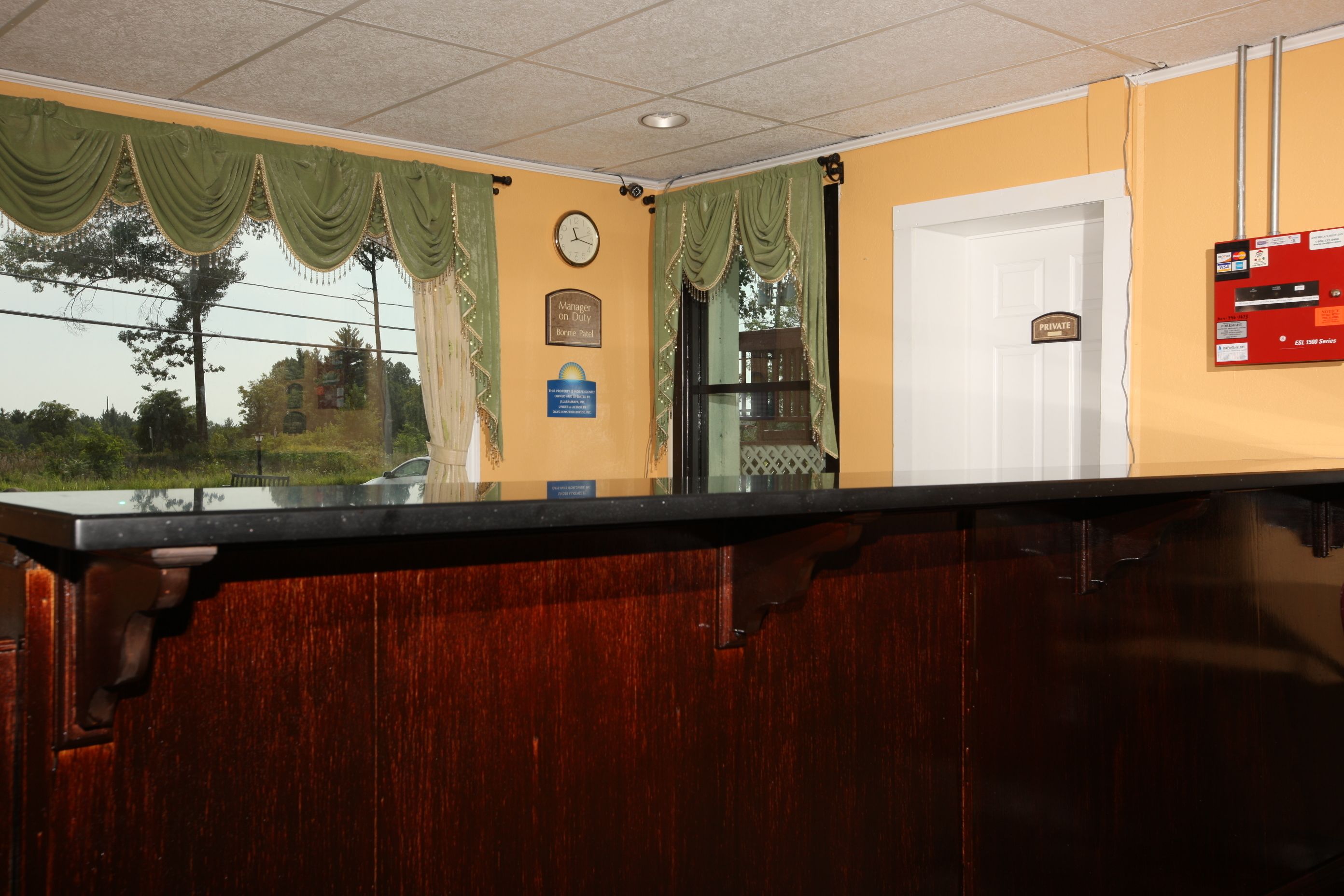 A reception area with a wooden counter, a clock, a private room sign, and a fire safety board.