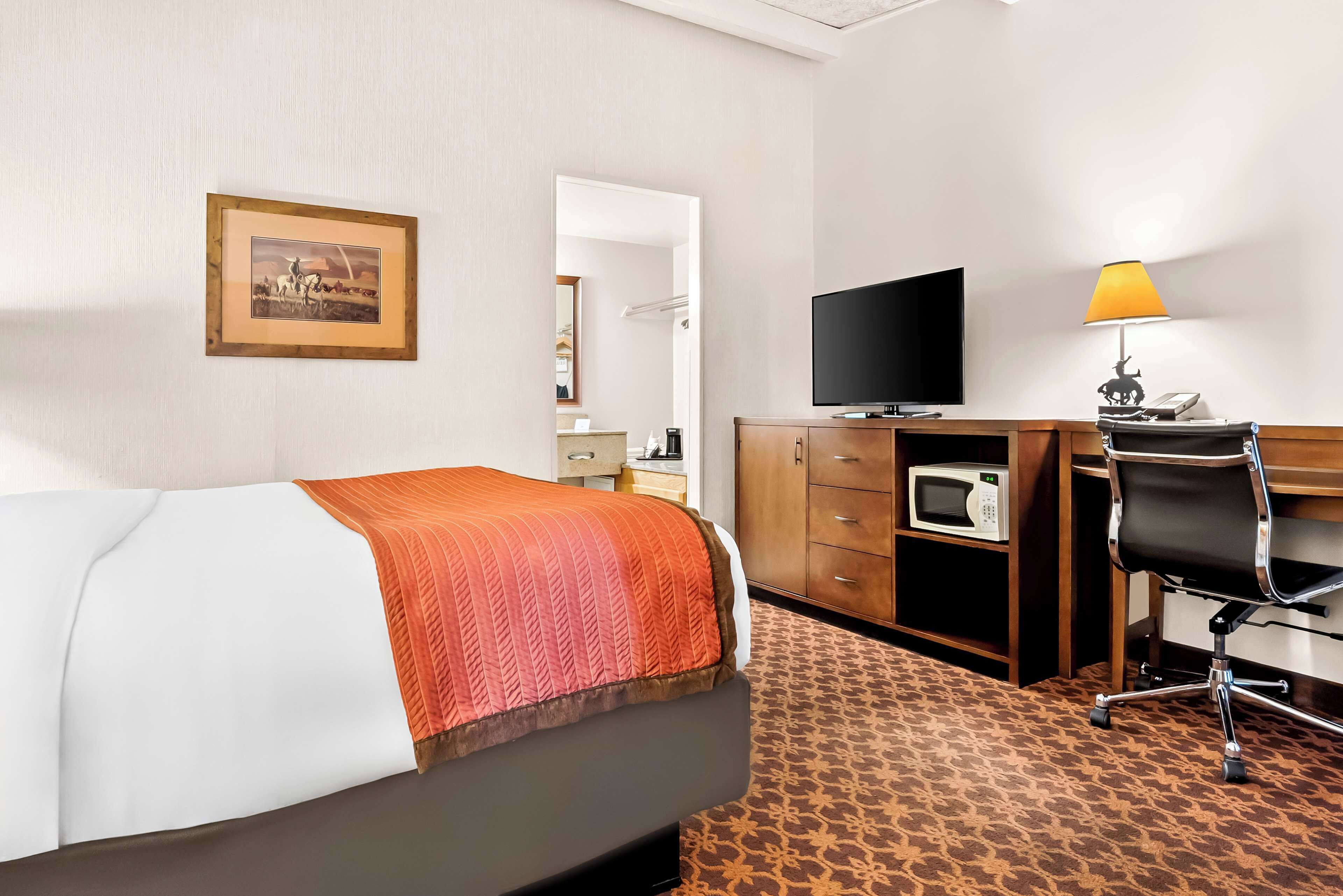 A hotel room with a bed, a desk with a computer, a television, and a microwave.