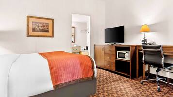 A hotel room with a bed, a desk with a computer, a television, and a microwave.