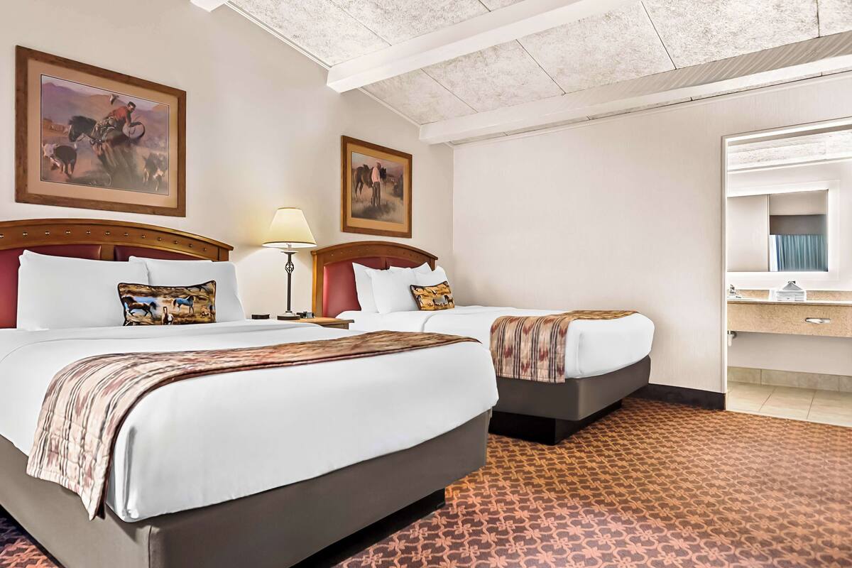 A hotel room with two beds, a large mirror, and artwork on the walls.