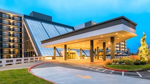 A modern hotel entrance with a covered walkway, large windows, and a well-lit facade. - Hilton Bellevue (Bellevue)
