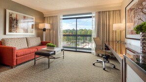 A hotel room with a red sofa, a desk, a chair, and a large window with a view of trees and buildings. - Hilton Bellevue (Bellevue)