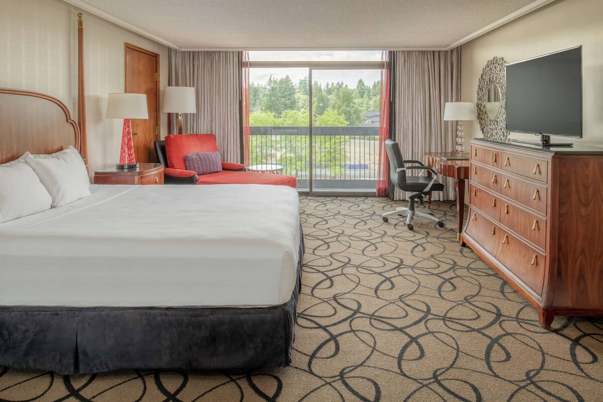 A hotel room with a large bed, a desk, a chair, a dresser, and a TV.