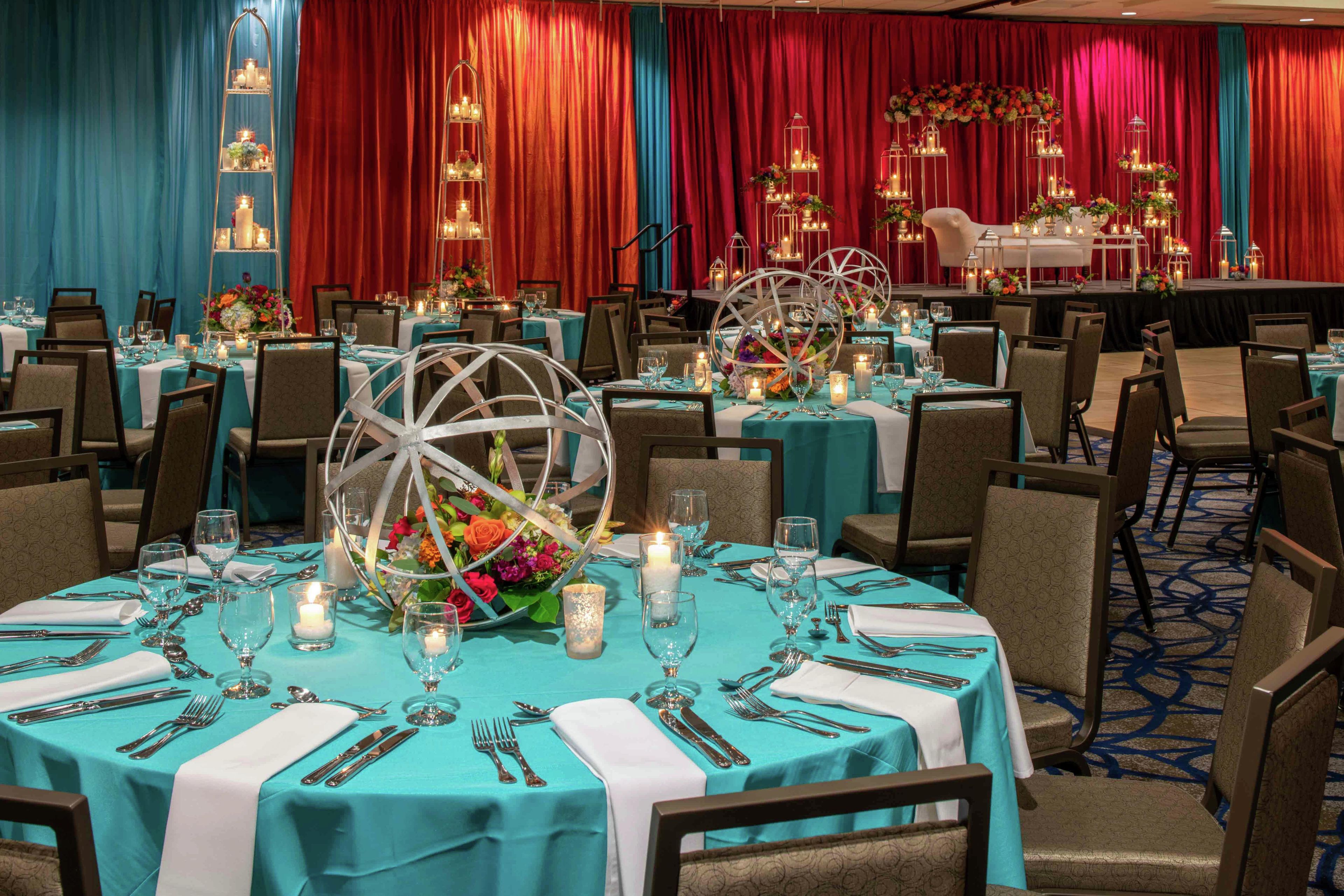 A banquet hall with round tables set for dining, featuring teal tablecloths, white napkins, and silverware.
