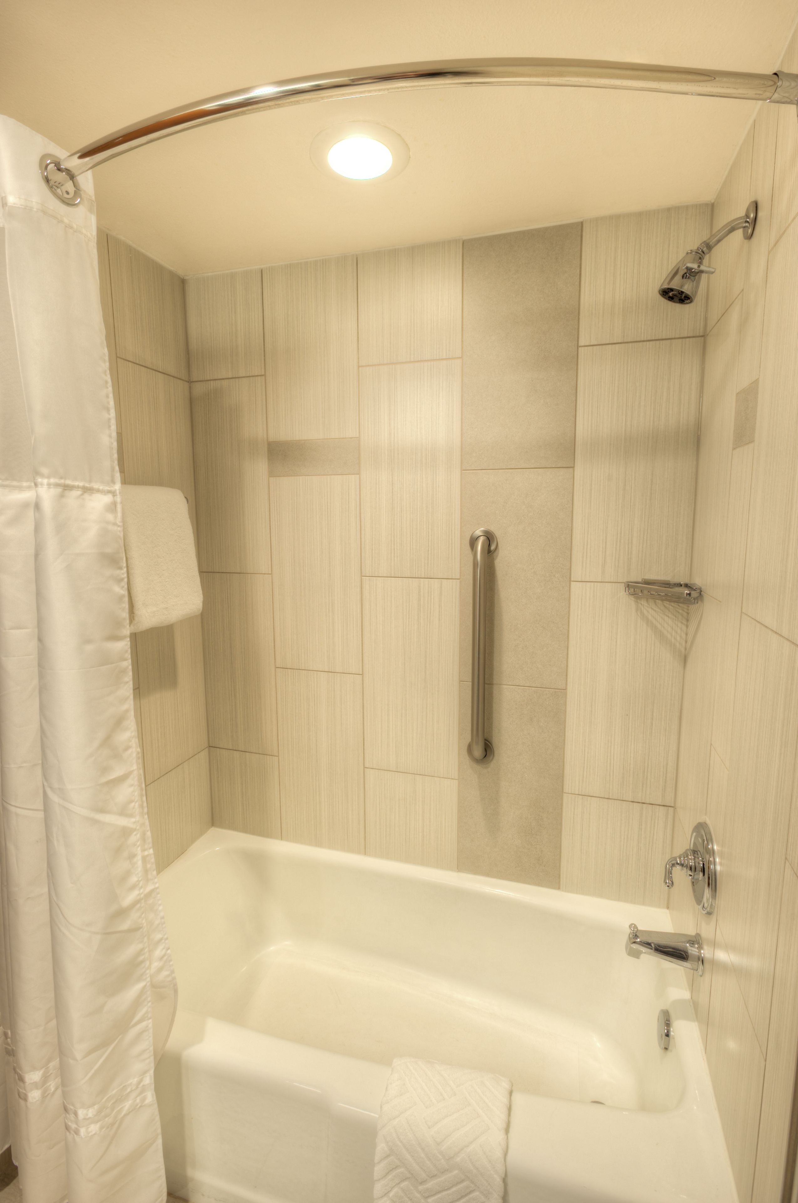 Ein modernes Badezimmer mit Badewanne, Dusche und Handläufer.