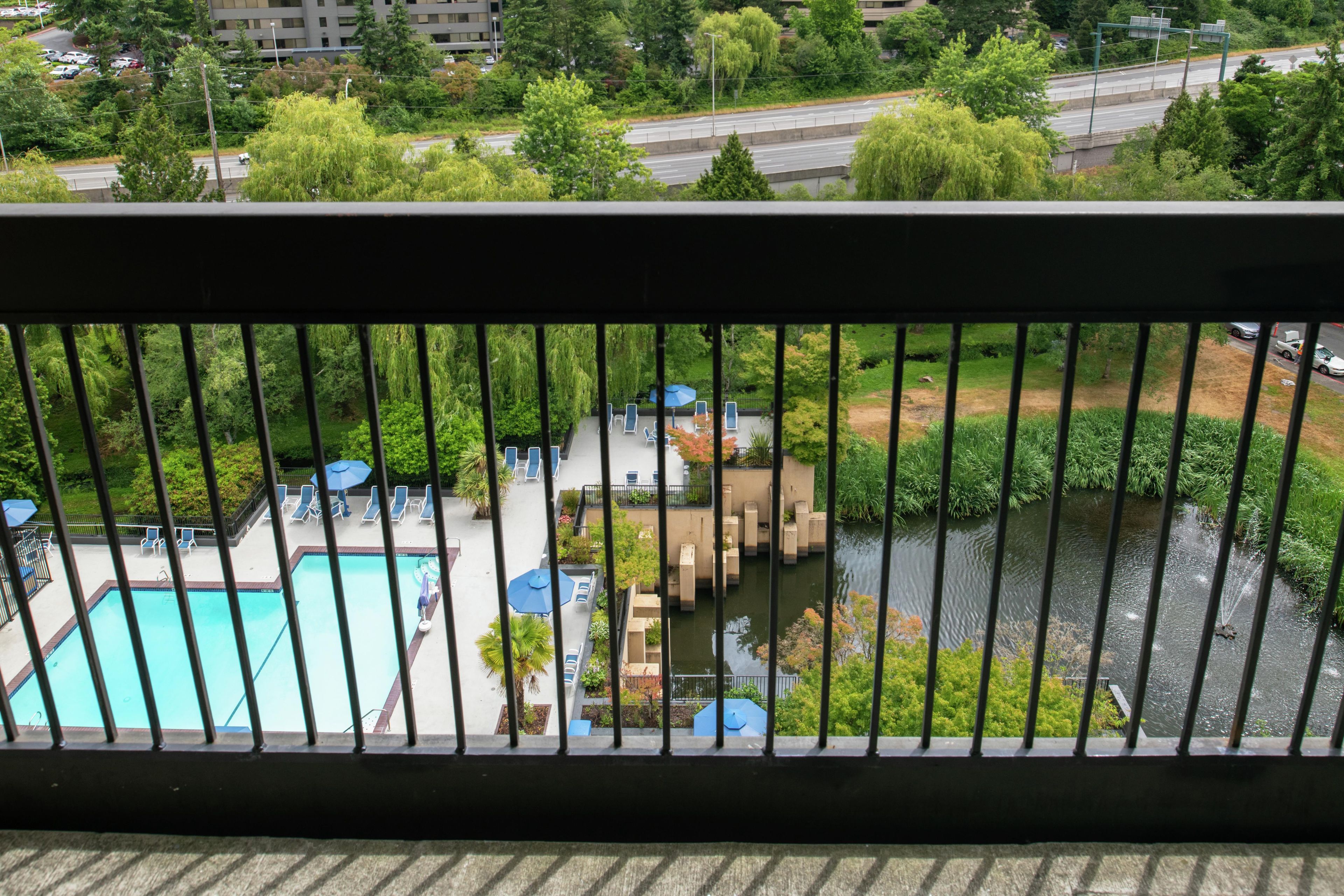A pool area with lounge chairs and umbrellas, surrounded by greenery and a river.