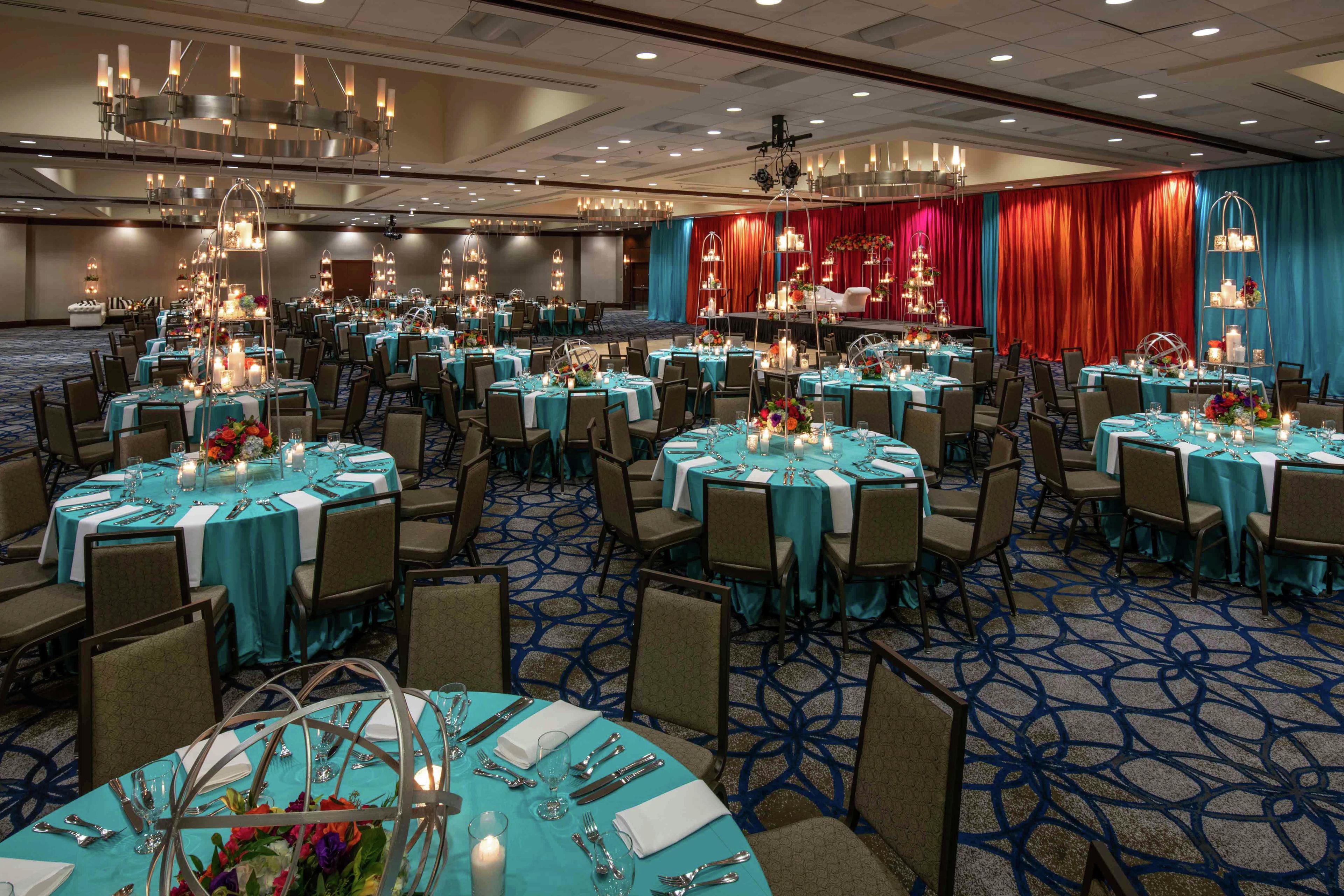 A banquet hall with round tables, chairs, and chandeliers.