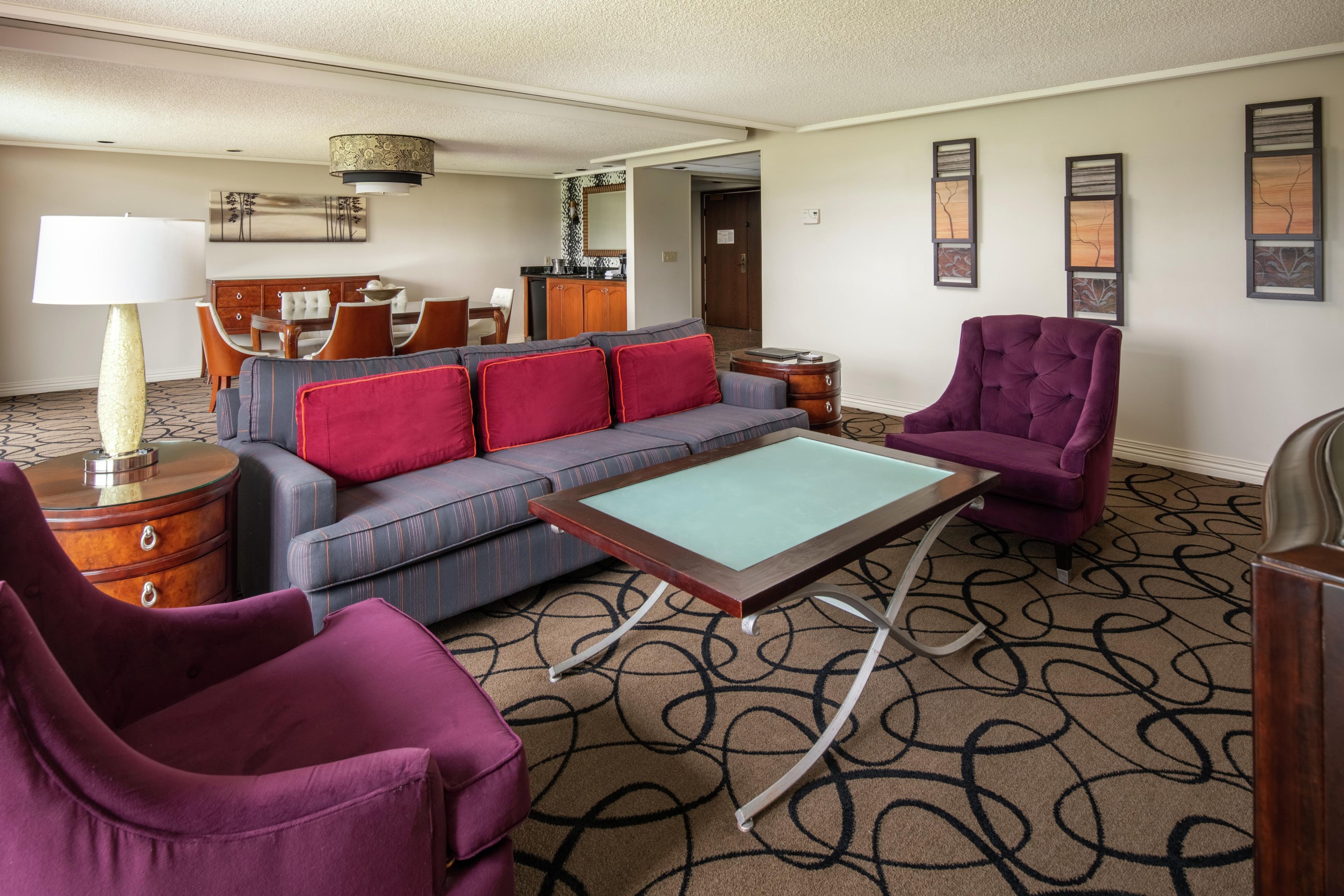 A hotel room with a sofa, armchairs, a pool table, a dining area, and artwork on the walls.