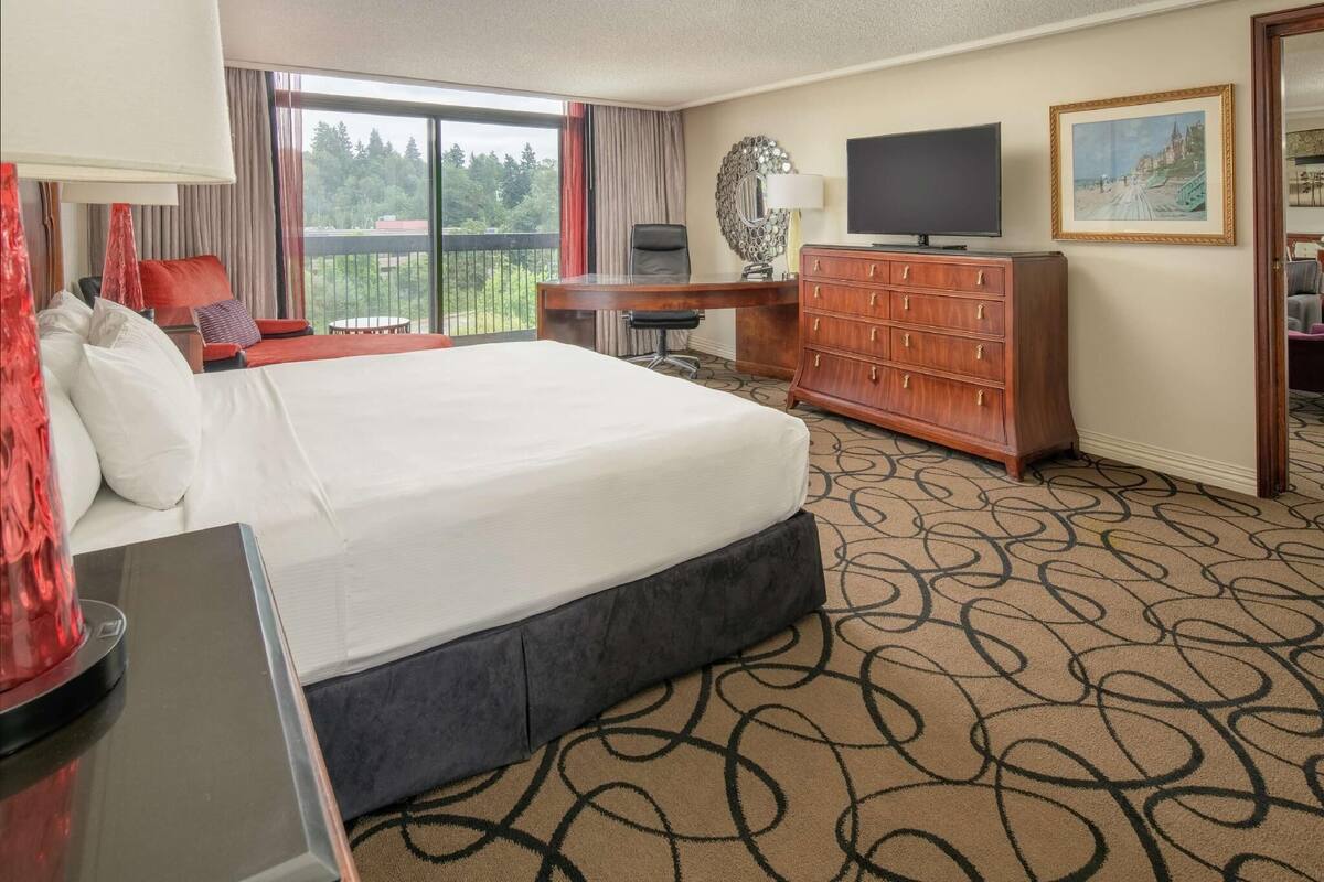 A hotel room with a large bed, a desk, a TV, and a view of the outdoors.