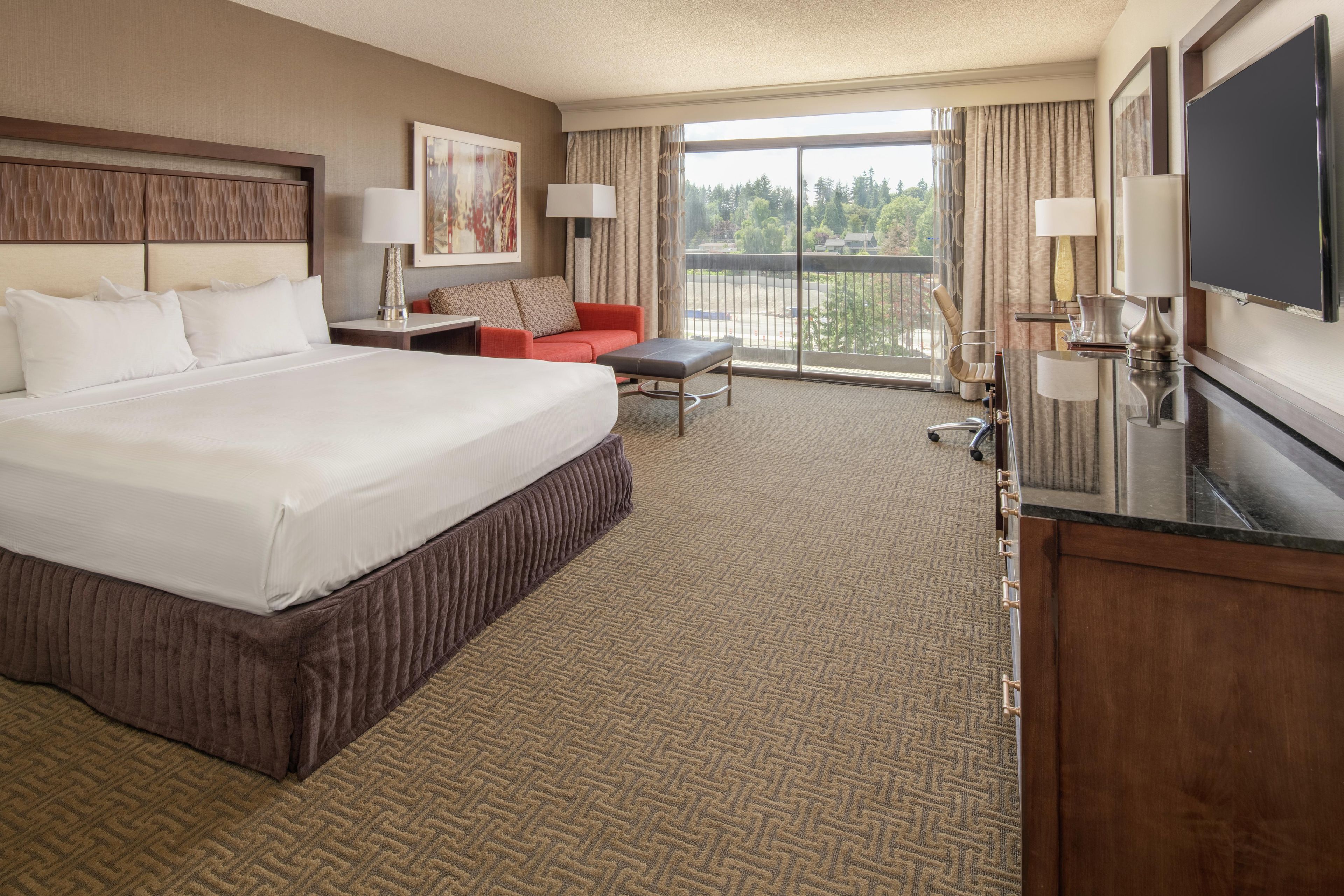 A hotel room with a large bed, a desk, a chair, a sofa, and a television.