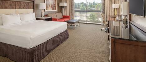 A hotel room with a large bed, a desk, a chair, a sofa, and a television.