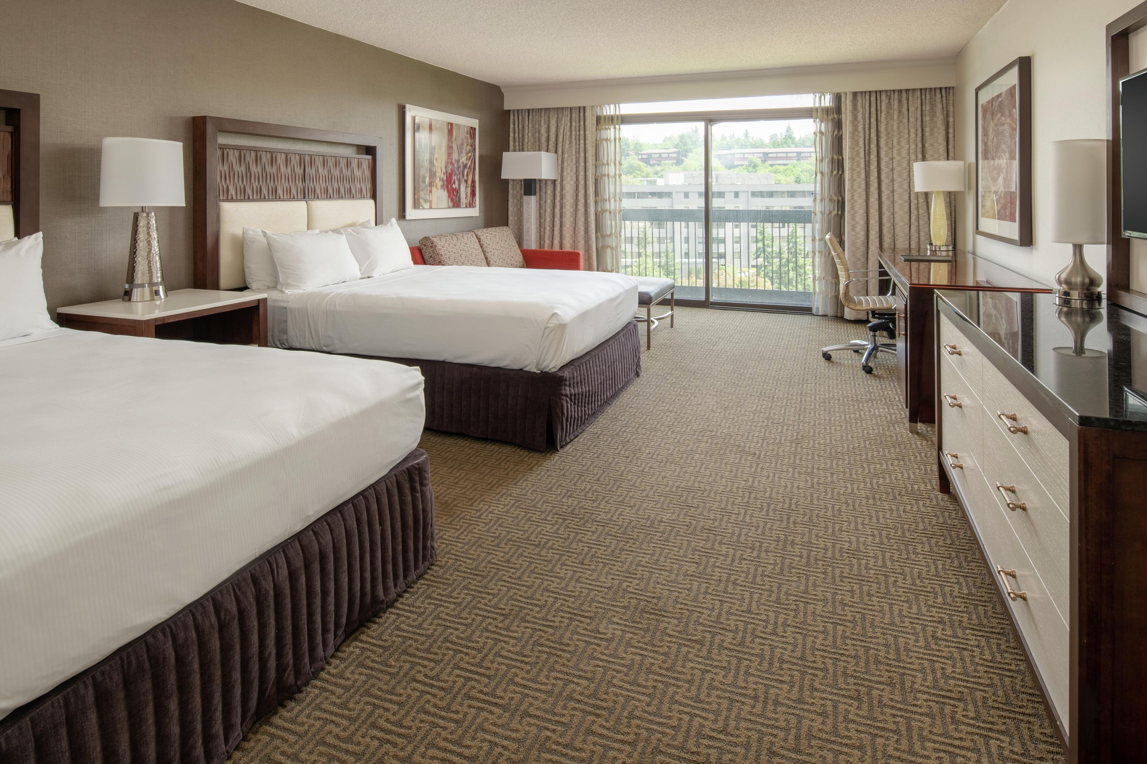 A hotel room with two beds, a desk, a chair, a dresser, and a balcony with a view.